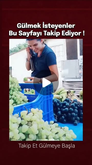 Videoda, bir meyve tezgahının önünde telefonla konuşurken dalgınlıkla elindeki yeşil eriği ısırmak y…